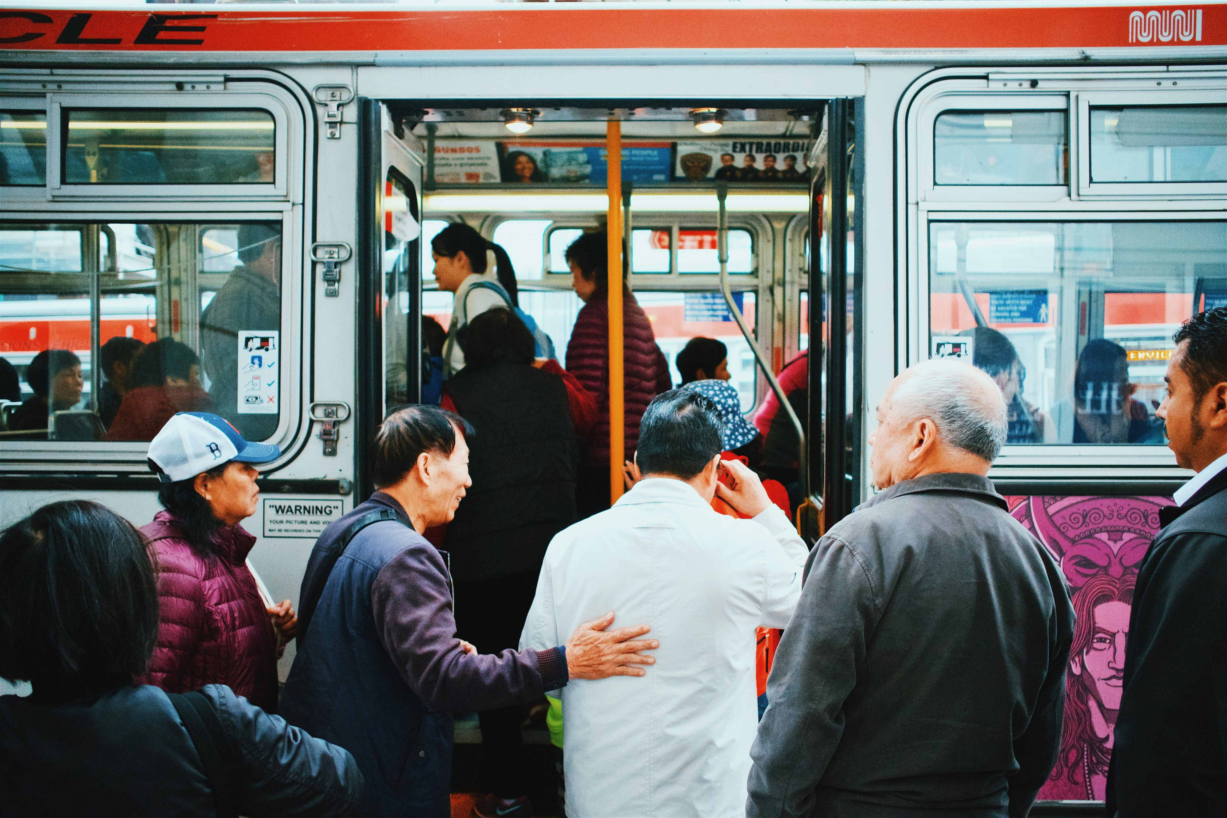 People boarding a crowded city bus during daytime, showcasing public transportation usage and diverse commuters in an urban setting.