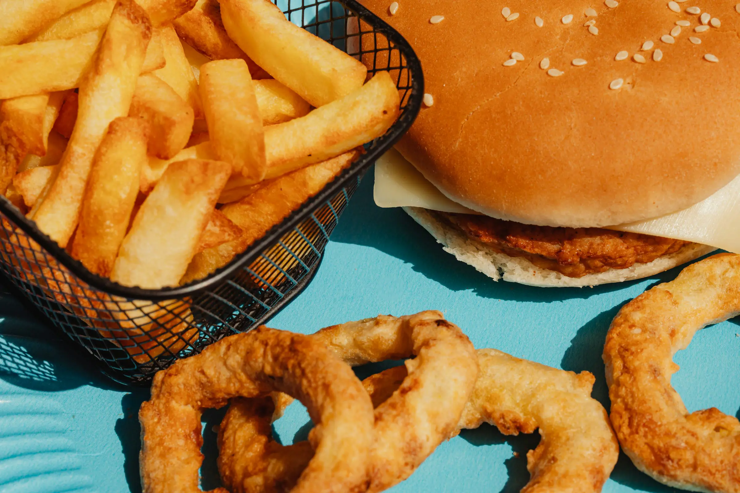 Hamburgare med pommes frites och lökringar på ett blått bord.
