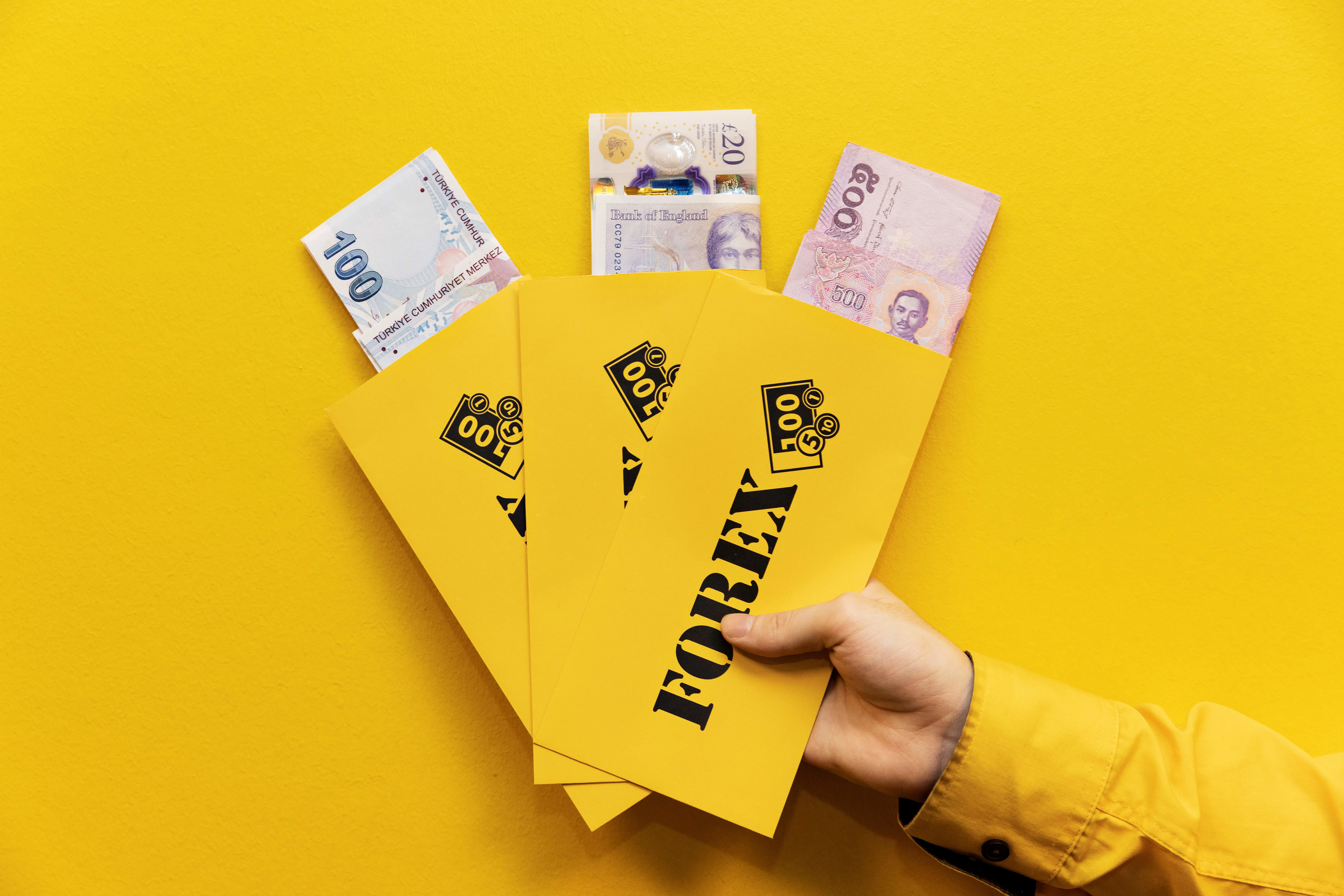 Hand holding envelopes marked "FOREX" with different currencies visible, against a yellow background.