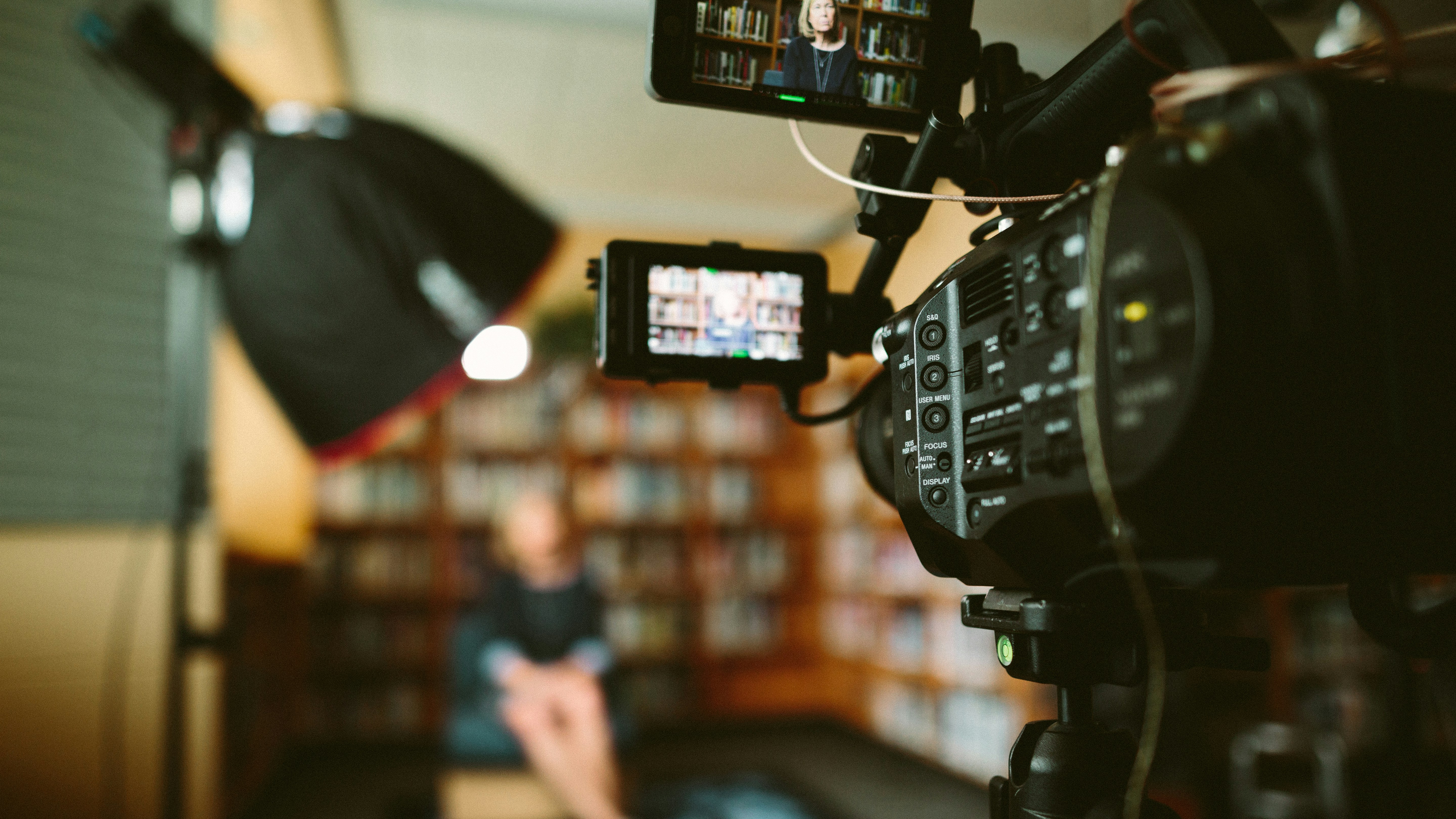 Professional video camera setup for filming an interview in a library setting, with studio lighting and a blurred background.