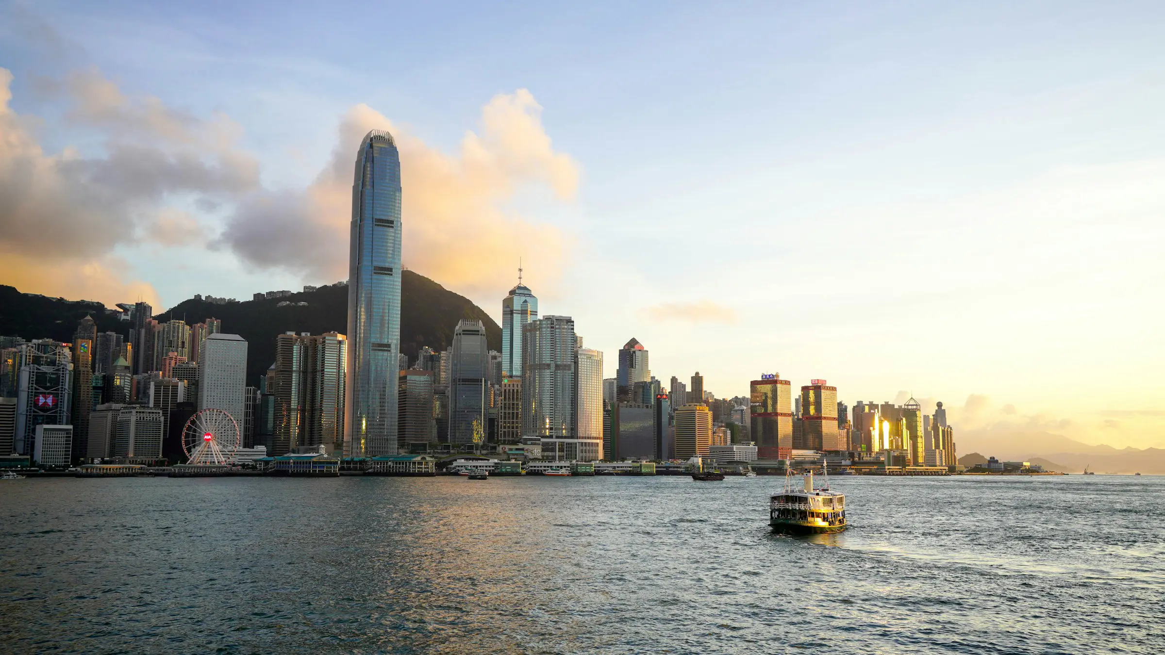 Hong Kong skyline at sunset with Victoria Harbour and ferry in the foreground.